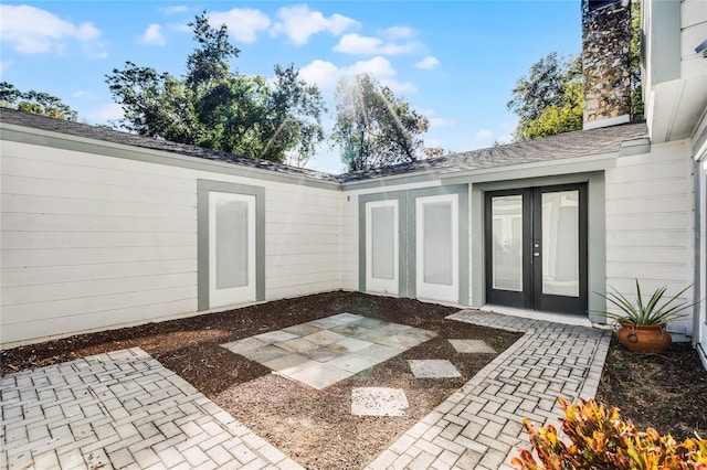 property entrance featuring a patio area, a shingled roof, a chimney, and french doors