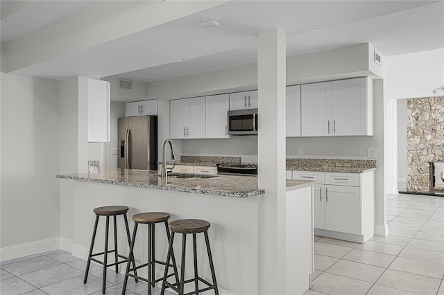 kitchen featuring light stone counters, a breakfast bar area, visible vents, appliances with stainless steel finishes, and a sink