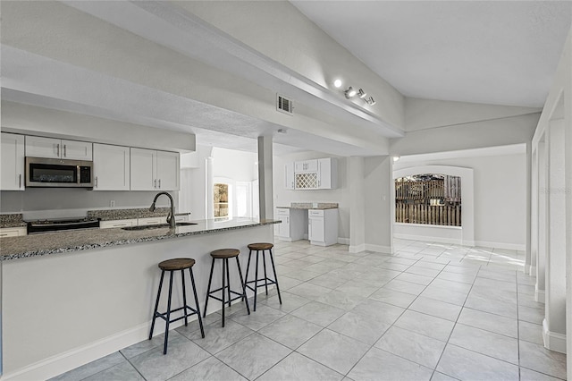 kitchen featuring visible vents, dark stone counters, lofted ceiling, appliances with stainless steel finishes, and a sink