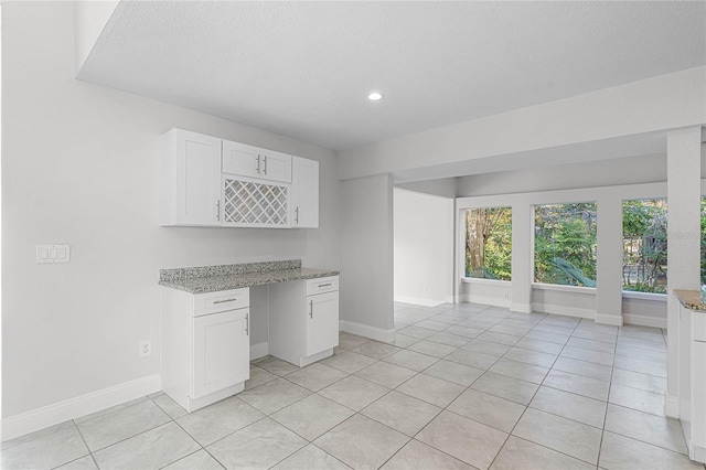 kitchen featuring baseboards, light tile patterned flooring, and white cabinets