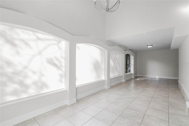 spare room with arched walkways, an inviting chandelier, baseboards, and light tile patterned floors