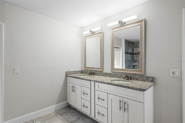 full bath featuring double vanity, tile patterned flooring, a sink, and baseboards