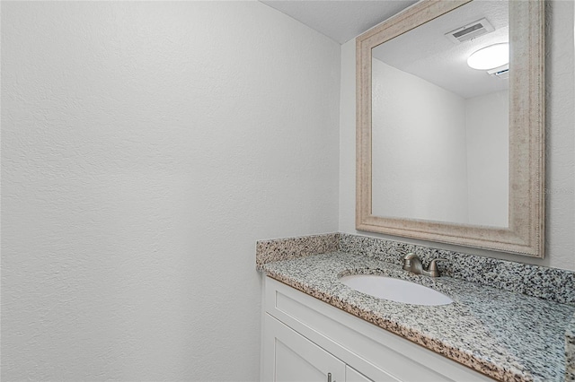 bathroom with visible vents, a textured wall, and vanity