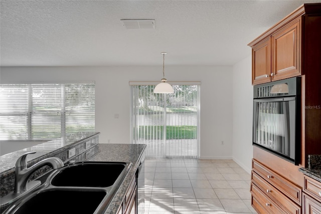 kitchen with wall oven, sink, light tile patterned floors, and dark stone counters