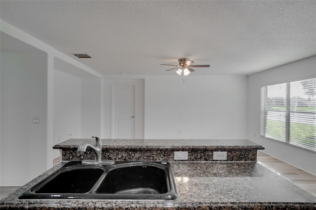 kitchen featuring sink, a textured ceiling, light hardwood / wood-style flooring, stone counters, and ceiling fan