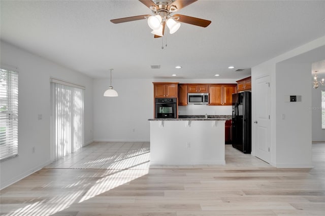 kitchen with a breakfast bar area, decorative light fixtures, light hardwood / wood-style flooring, ceiling fan with notable chandelier, and black appliances