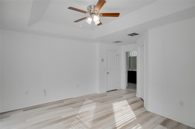 empty room with ceiling fan, a tray ceiling, and light hardwood / wood-style floors