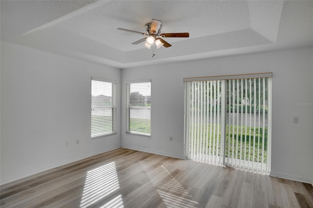 spare room featuring light hardwood / wood-style flooring, a textured ceiling, ceiling fan, and a tray ceiling