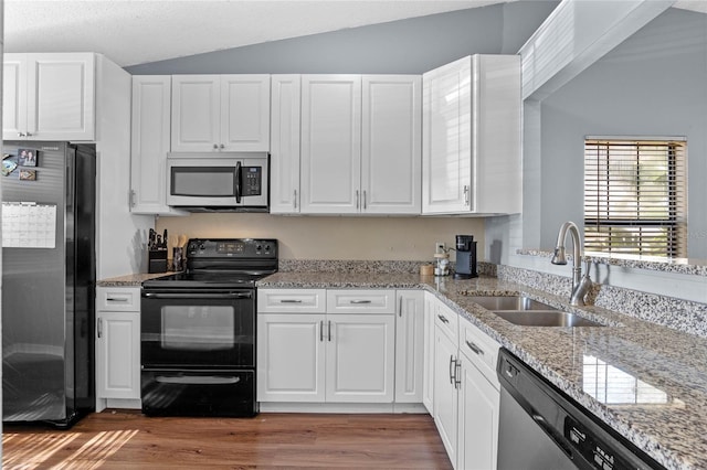 kitchen with lofted ceiling, white cabinets, sink, light stone countertops, and appliances with stainless steel finishes