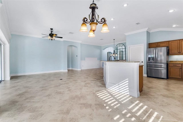 kitchen featuring stainless steel fridge, hanging light fixtures, light stone counters, ornamental molding, and a center island with sink