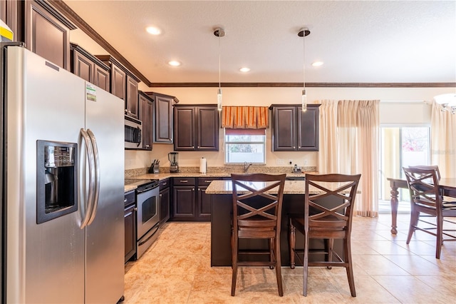 kitchen featuring dark brown cabinetry, a center island, hanging light fixtures, stainless steel appliances, and light stone counters