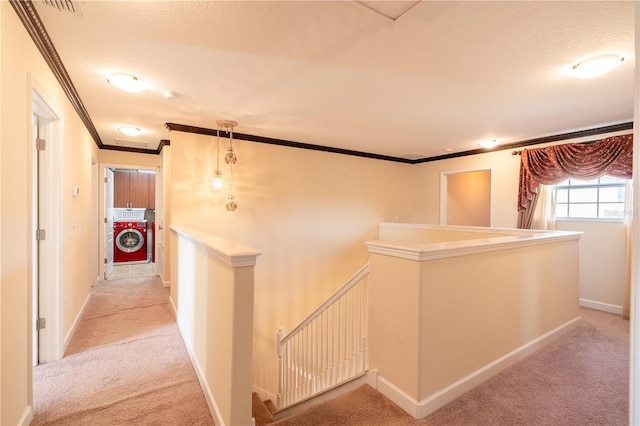 hallway with washer / clothes dryer, light colored carpet, a textured ceiling, and ornamental molding