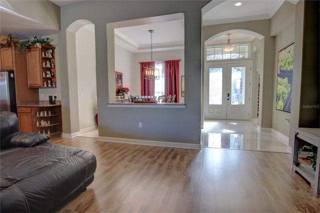 entrance foyer with french doors, an inviting chandelier, ornamental molding, a tray ceiling, and light hardwood / wood-style floors