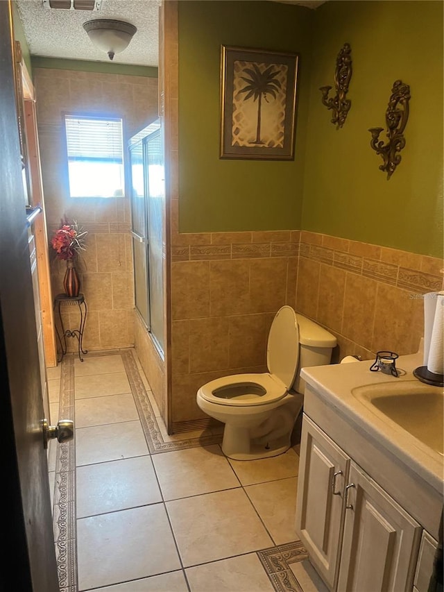 bathroom with a shower with door, tile patterned flooring, toilet, a textured ceiling, and tile walls