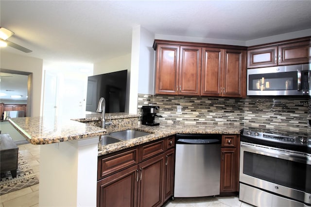 kitchen with sink, light stone counters, backsplash, kitchen peninsula, and appliances with stainless steel finishes