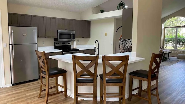 kitchen with light hardwood / wood-style flooring, a textured ceiling, lofted ceiling, a breakfast bar, and appliances with stainless steel finishes