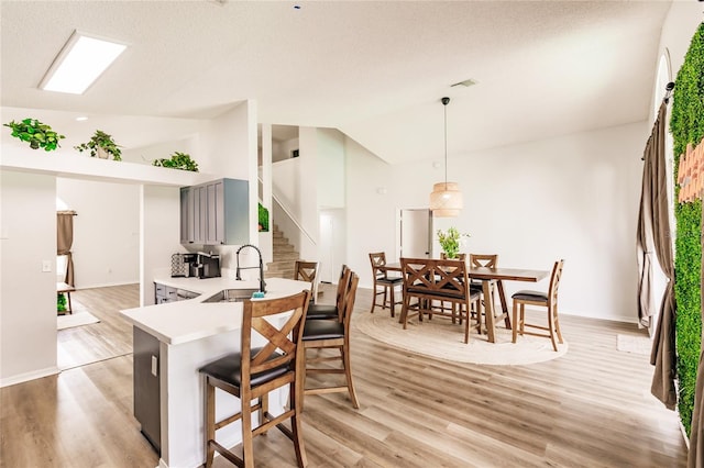 kitchen featuring lofted ceiling, a breakfast bar, a sink, light wood-style floors, and light countertops