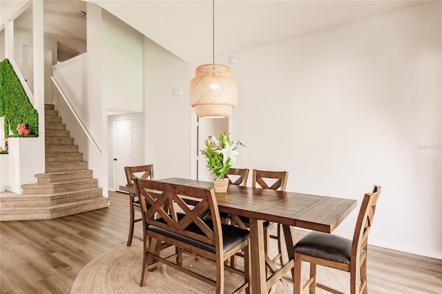 dining space with light wood-type flooring, stairway, and a towering ceiling