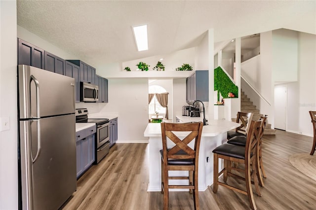 kitchen with light countertops, appliances with stainless steel finishes, vaulted ceiling, light wood-type flooring, and a kitchen bar