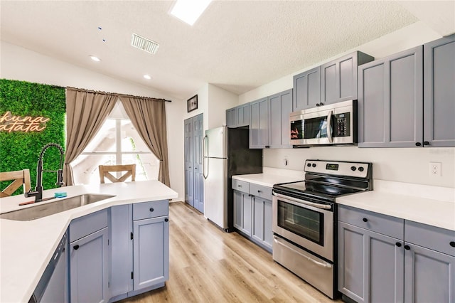 kitchen with gray cabinetry, stainless steel appliances, a sink, visible vents, and vaulted ceiling