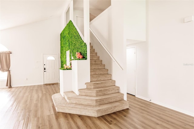 stairs with baseboards, high vaulted ceiling, and wood finished floors