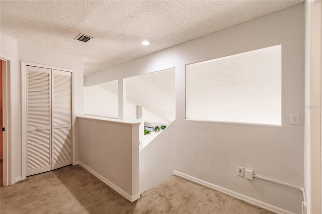 corridor with a healthy amount of sunlight, carpet flooring, visible vents, and an upstairs landing