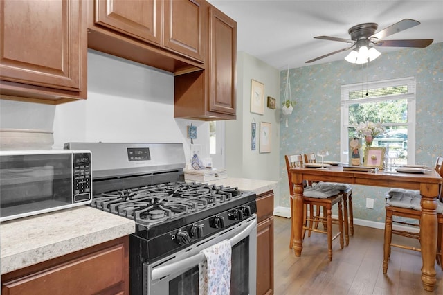 kitchen with stainless steel gas range oven, ceiling fan, and light hardwood / wood-style flooring