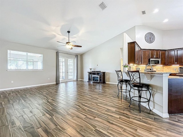 kitchen with french doors, a kitchen breakfast bar, light stone counters, dark hardwood / wood-style floors, and dark brown cabinets