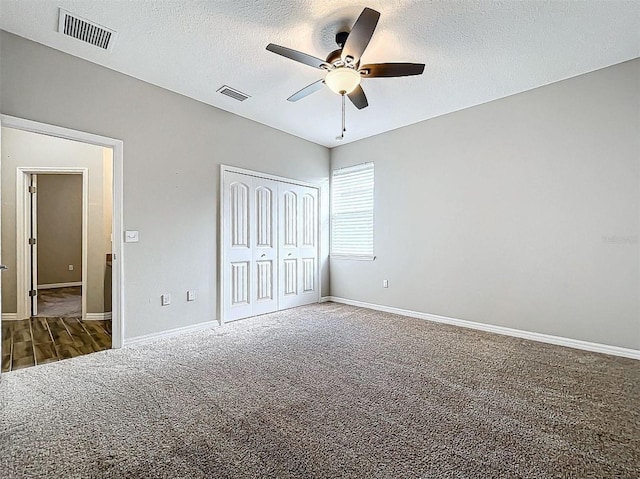 unfurnished bedroom with dark colored carpet, ceiling fan, a textured ceiling, and a closet