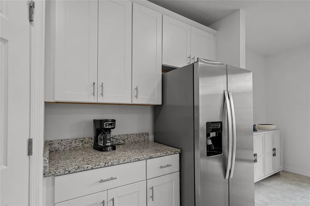 kitchen with stainless steel fridge, white cabinets, light stone counters, and light tile patterned floors