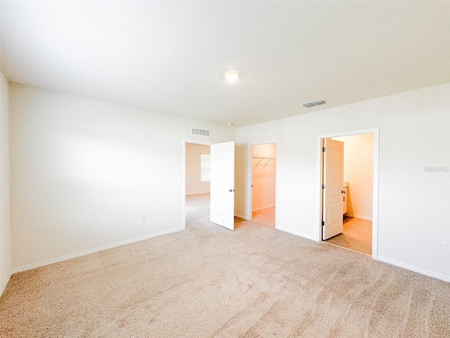 unfurnished bedroom with a closet, light colored carpet, a walk in closet, and ensuite bath