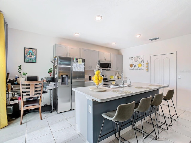 kitchen with a kitchen bar, appliances with stainless steel finishes, gray cabinetry, a kitchen island with sink, and sink