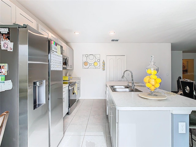 kitchen featuring white cabinets, a center island with sink, sink, appliances with stainless steel finishes, and light tile patterned flooring