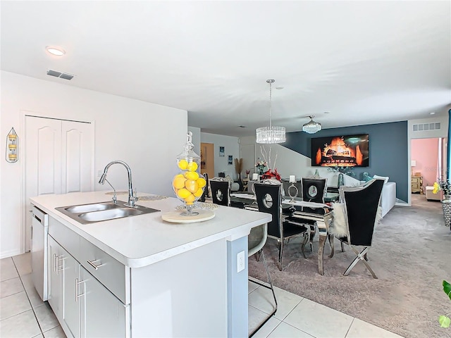 kitchen with stainless steel dishwasher, sink, a center island with sink, a chandelier, and hanging light fixtures