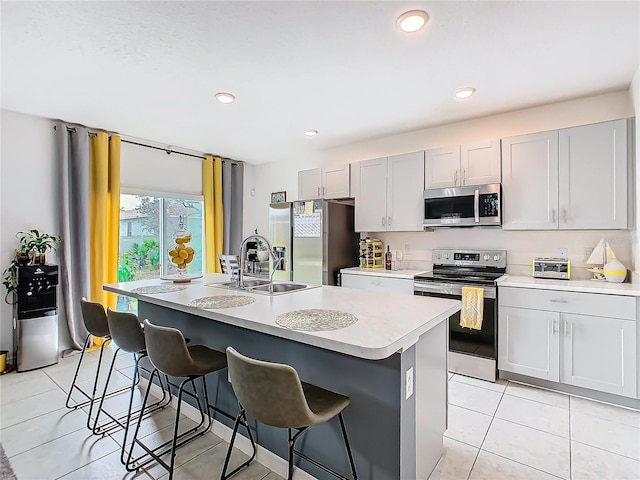 kitchen with sink, stainless steel appliances, a kitchen bar, a kitchen island with sink, and light tile patterned floors