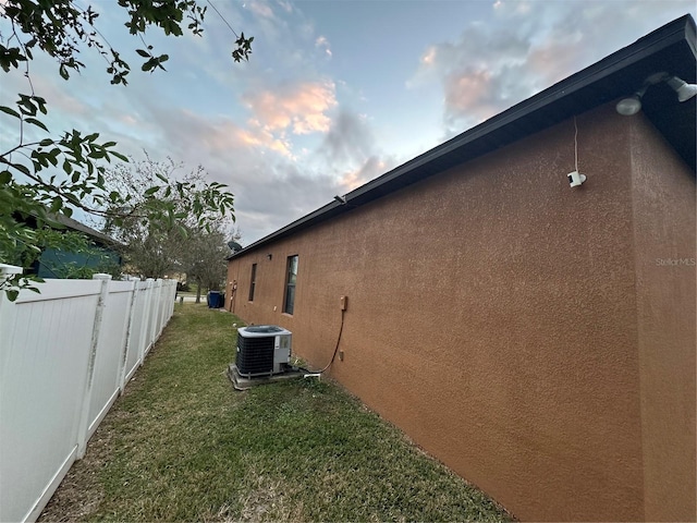 property exterior at dusk with a lawn and cooling unit