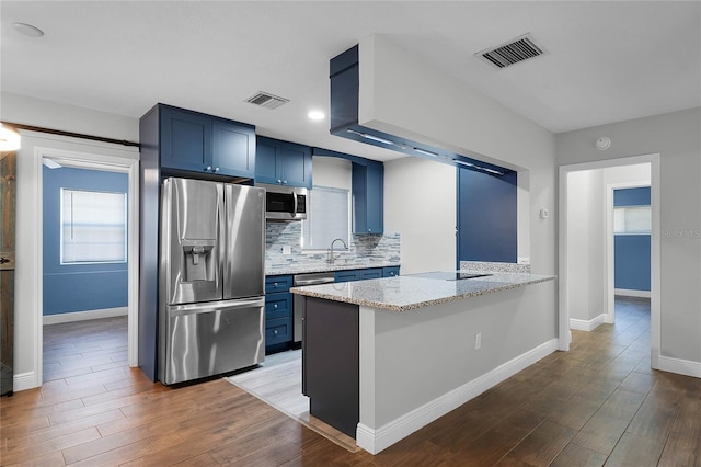 kitchen with light stone counters, blue cabinets, kitchen peninsula, appliances with stainless steel finishes, and hardwood / wood-style flooring