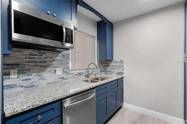 kitchen featuring blue cabinetry, stainless steel appliances, light stone counters, and sink