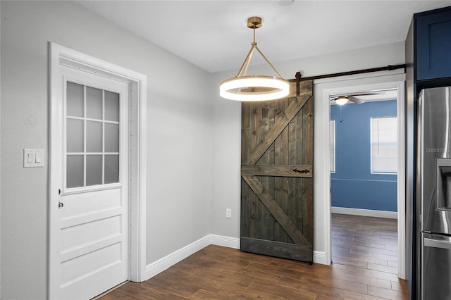 unfurnished dining area featuring a barn door, ceiling fan, and dark wood-type flooring