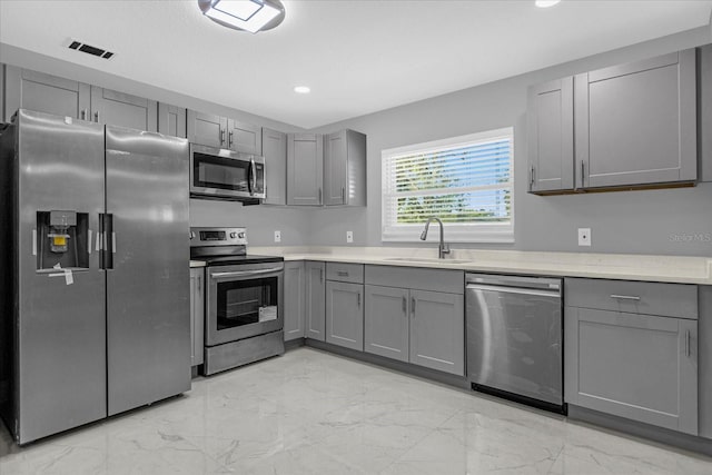 kitchen with stainless steel appliances, gray cabinetry, and sink