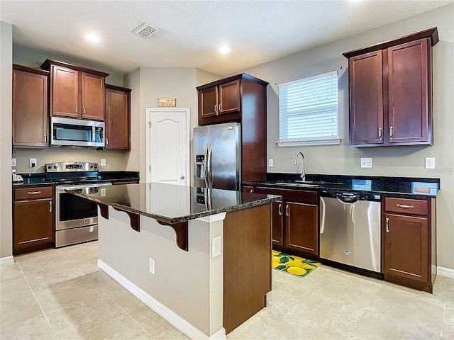 kitchen with sink, a breakfast bar area, dark stone countertops, a kitchen island, and stainless steel appliances