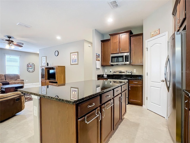 kitchen with ceiling fan, a center island, dark stone countertops, light tile patterned floors, and appliances with stainless steel finishes