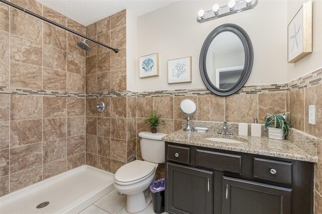 bathroom with a tile shower, vanity, tile walls, and toilet