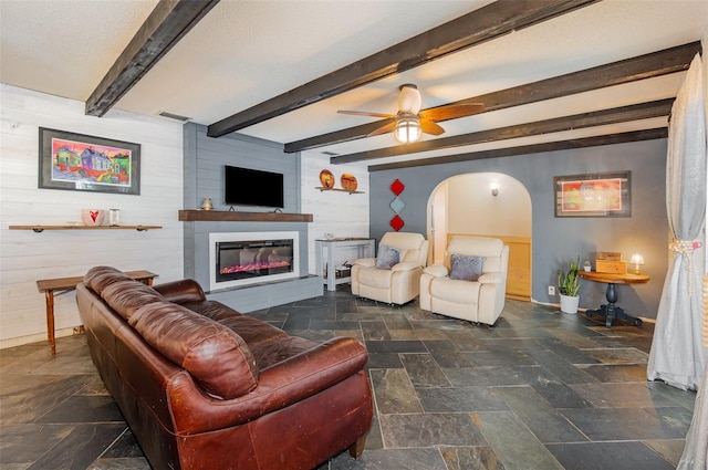 living room with beamed ceiling, ceiling fan, and wood walls