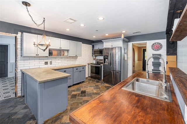 kitchen featuring butcher block countertops, sink, appliances with stainless steel finishes, hanging light fixtures, and white cabinets