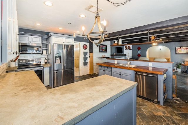 kitchen featuring pendant lighting, sink, appliances with stainless steel finishes, gray cabinetry, and wood counters