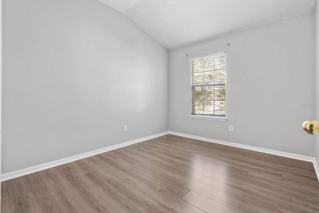 spare room with baseboards, wood finished floors, and vaulted ceiling