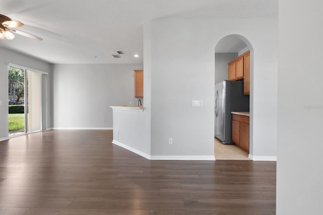 unfurnished living room featuring arched walkways, baseboards, ceiling fan, and wood finished floors