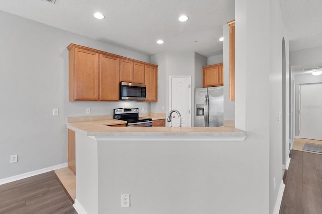 kitchen featuring baseboards, light countertops, light wood-type flooring, recessed lighting, and appliances with stainless steel finishes