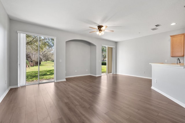 unfurnished living room with arched walkways, dark wood-style floors, baseboards, and ceiling fan